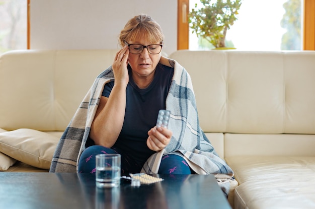 Una donna di mezza età tiene in mano un blister di pillole e legge le istruzioni mediche seduta sul divano