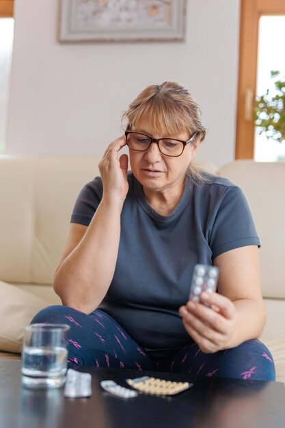 Una donna di mezza età tiene in mano un blister di pillole e legge le istruzioni mediche seduta sul divano