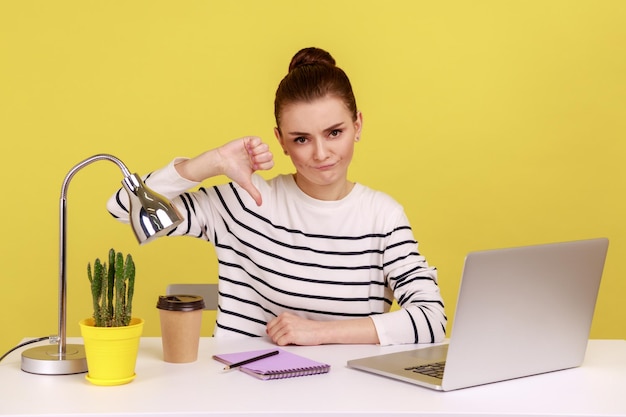 Una donna dispiaciuta che lavora in un ufficio mostra il pollice verso il basso, un gesto che esprime disapprovazione.