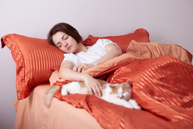 Una donna dorme in un letto con il gatto vicino.