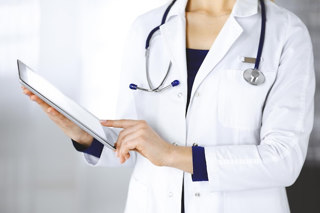 Una donna-dottore sconosciuta tiene in mano un tablet computer, mentre è in piedi in una clinica. Una medico donna con uno stetoscopio nel suo ufficio, close-up. Servizio medico perfetto in un ospedale. Medicina