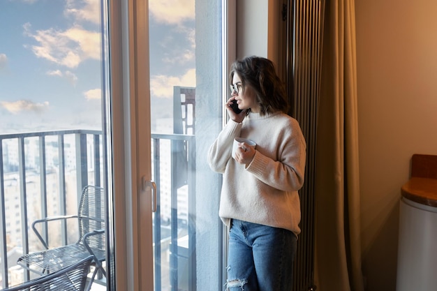 Una donna è in piedi davanti a un balcone e parla al telefono.