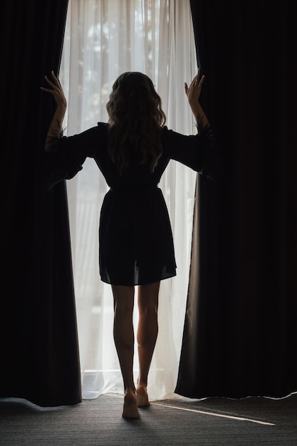 Una donna è in piedi davanti a una finestra da cui splende il sole.