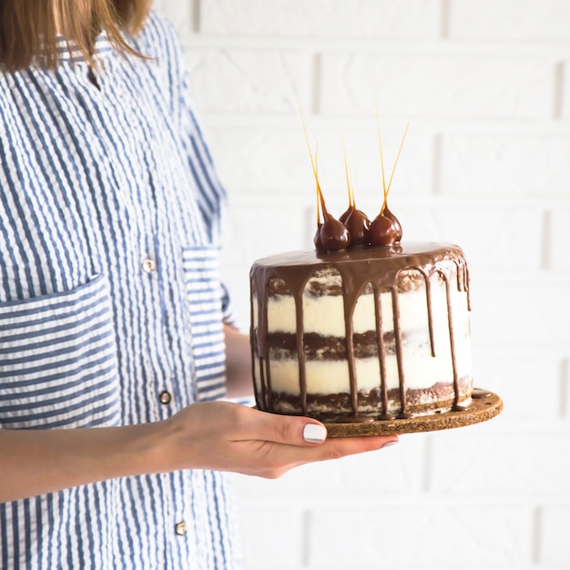 Una donna è in possesso di una piccola torta rotonda bella piena di cioccolato