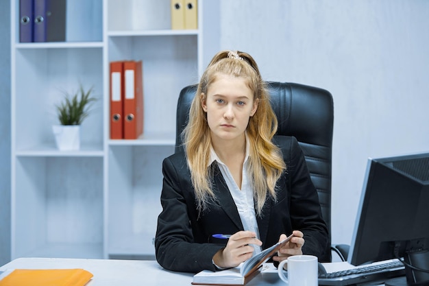 Una donna è seduta alla sua scrivania in ufficio e guarda la telecamera