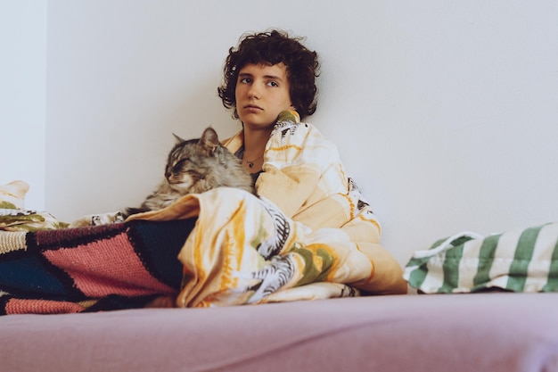 Una donna è seduta su un letto con un gatto in grembo.