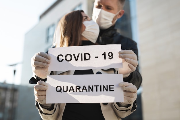 Una donna e un uomo in maschera medica protettiva reggono un cartello con le parole Quarantine e Covid 19