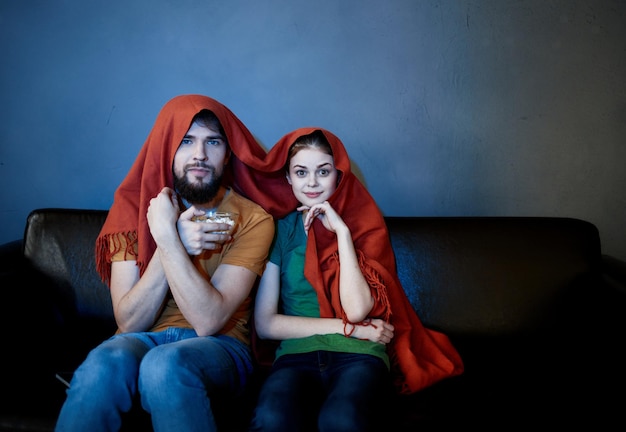 una donna e un uomo sotto una coperta rossa sul divano a guardare la tv la sera