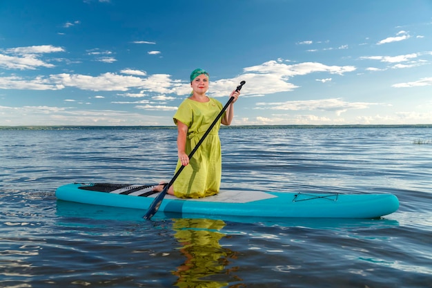 Una donna ebrea con un vestito e un copricapo kisui rosh su una tavola SUP inginocchiata galleggia sul lago