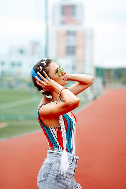 Una donna elegante in occhiali da sole e cuffie grandi ascolta musica allo stadio.