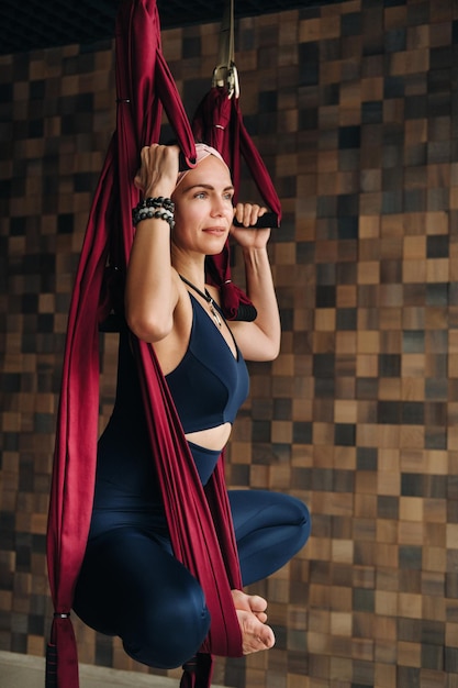 Una donna fa yoga su un'amaca appesa bordeaux in palestra