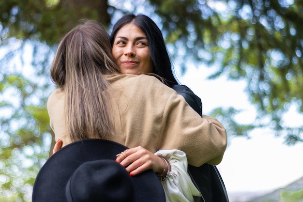 Una donna felice che abbraccia la sua amica nel parco mentre tiene il suo cappello