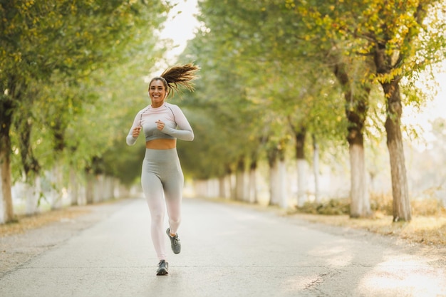 Una donna felice che indossa abiti sportivi corre lungo il sentiero soleggiato del viale.