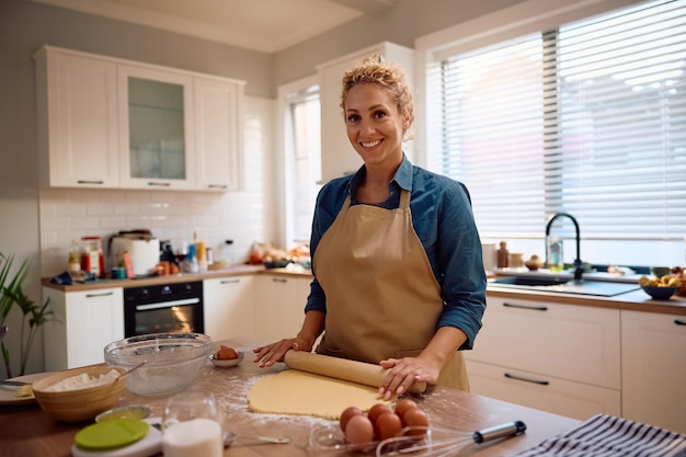 Una donna felice che usa un rotolino mentre prepara la pasta e cuoce in cucina