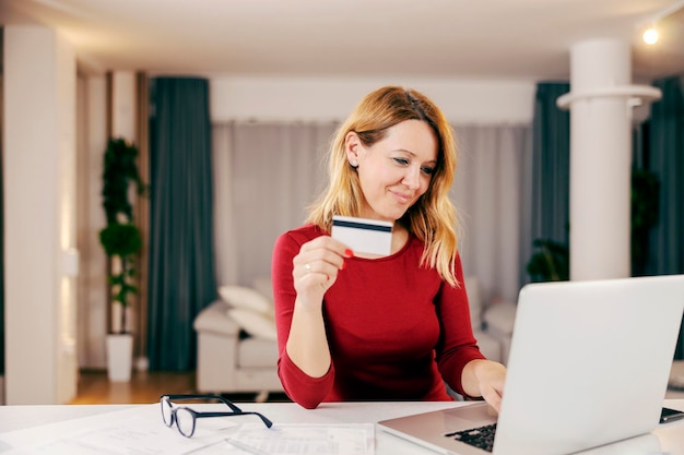 Una donna felice che utilizza la carta di credito per la prenotazione dello shopping online di pagare le bollette da casa confortevole