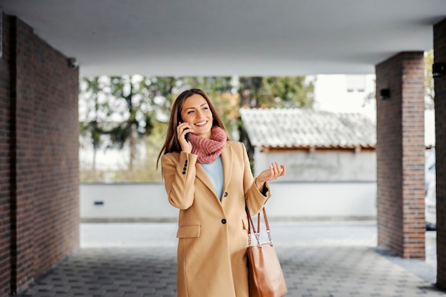 Una donna felice con un cappotto che cammina all'aperto e conversa al telefono T