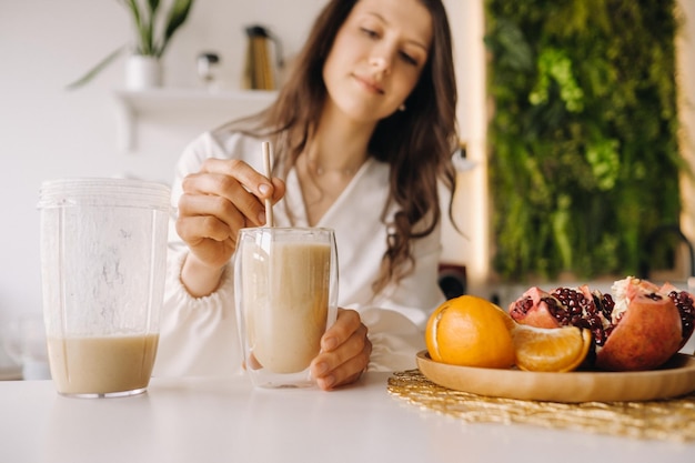 Una donna felice e sana ha preparato un cocktail di frutta in piedi in cucina a casaMangiare sano