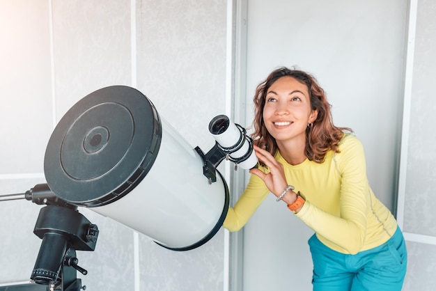 Una donna felice in un osservatorio spaziale guarda un meteorite o il sole attraverso un telescopio ottico professionale Occupazione astronomica e concetto di studio