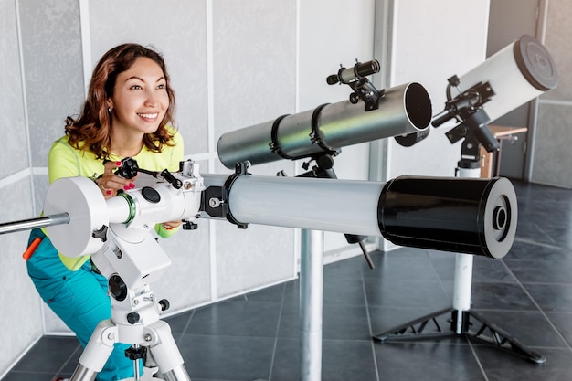 Una donna felice in un osservatorio spaziale guarda un meteorite o il sole attraverso un telescopio ottico professionale Occupazione astronomica e concetto di studio