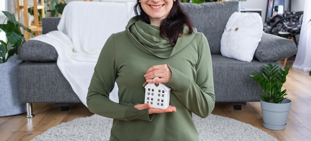 Una donna felice nella sua casa tiene tra le mani una figura in miniatura di una casa e una chiave all'interno Progetto casa da sogno acquisto immobiliare assicurazione mutuo prenotazione affitto