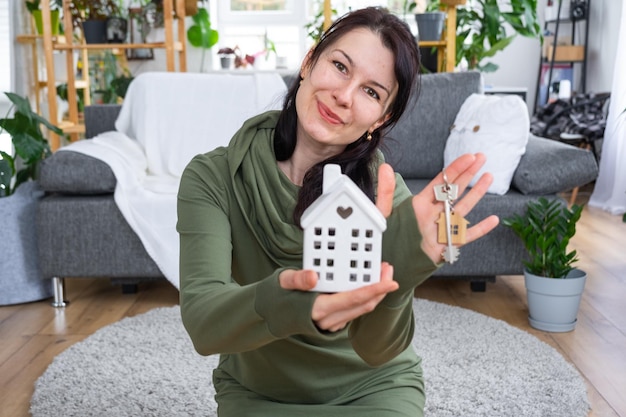 Una donna felice nella sua casa tiene tra le mani una figura in miniatura di una casa e una chiave all'interno Progetto casa da sogno acquisto immobiliare assicurazione mutuo prenotazione affitto