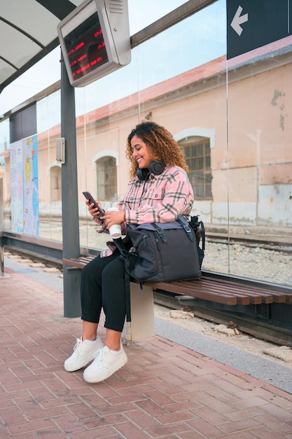 Una donna formosa con i capelli ricci guarda il suo telefono alla fermata del treno