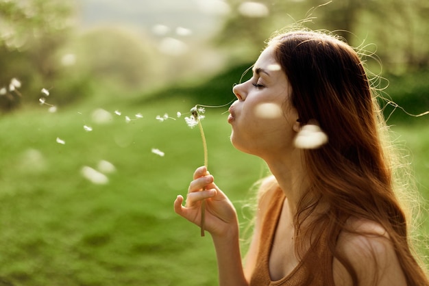 Una donna freelance passeggia spensierata e felice in un parco verdeggiante e soffia via un fiore di tarassaco alla luce del tramonto