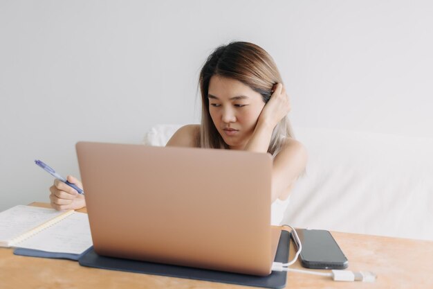 Una donna freelance seria sta lavorando online a casa con un computer portatile e prende appunti in lei