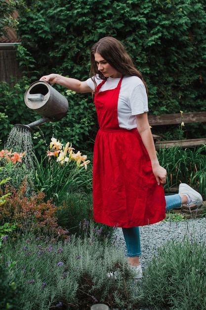 Una donna giardiniere con un grembiule rosso che innaffia il giardino