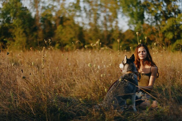 Una donna gioca e balla con un cane di razza husky in natura in autunno su un campo di erba addestrando e addestrando un giovane cane