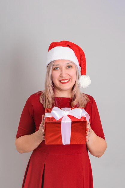 Una donna gioiosa con un cappello da Babbo Natale tiene in mano una scatola regalo rossa, foto verticale