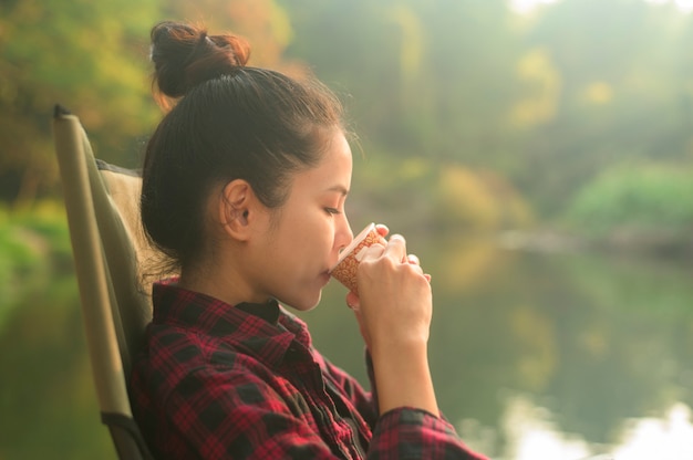 Una donna giovane e bella viaggiatrice sta godendo con la natura bere caffè al mattino sul lago