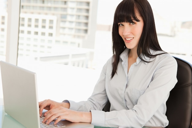 Una donna guarda la telecamera mentre digita sul suo laptop