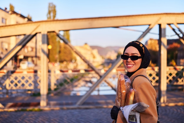 Una donna hijab in eleganti occhiali da sole e un elegante abito francese che cammina per la città al tramonto