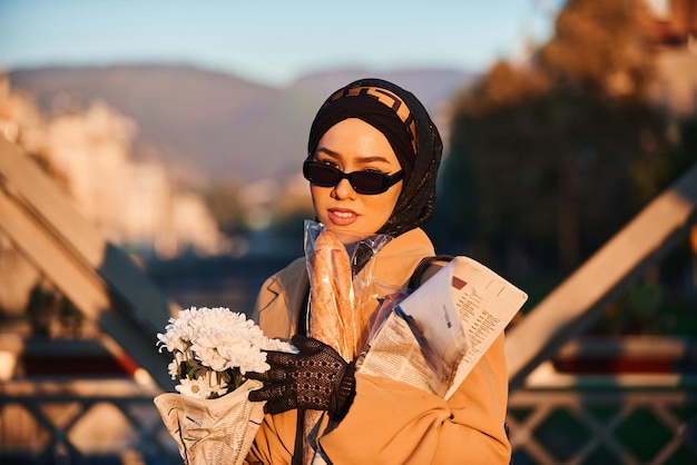 Una donna hijab in eleganti occhiali da sole e un elegante abito francese che cammina per la città al tramonto