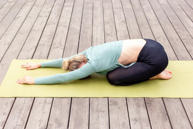 Una donna in abbigliamento sportivo su una piattaforma di legno in estate fa yoga