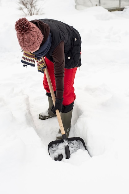 Una donna in abiti caldi che usa una pala di plastica nera con un manico di legno fa il percorso nella neve