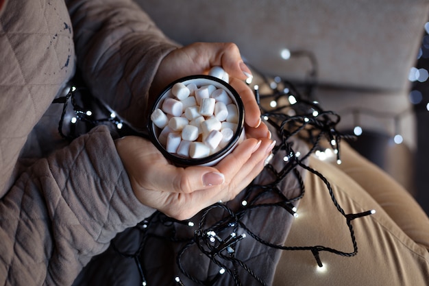 Una donna in abiti caldi con una ghirlanda di Natale in ginocchio si scalda