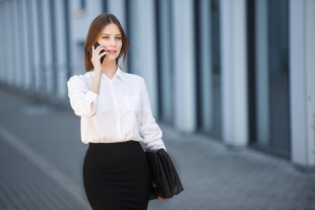 Una donna in abiti d'affari va in ufficio parlando al telefono con una cartella di documenti Copia spazio