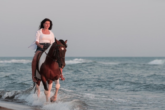 Una donna in abiti estivi si diverte a cavalcare su una bellissima spiaggia sabbiosa al tramonto. Messa a fuoco selettiva. Foto di alta qualità