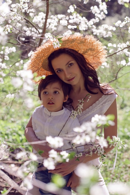 Una donna in abiti rosa e un cappello di paglia sta con un bambino in una camicia bianca in un frutteto di mele in fiore