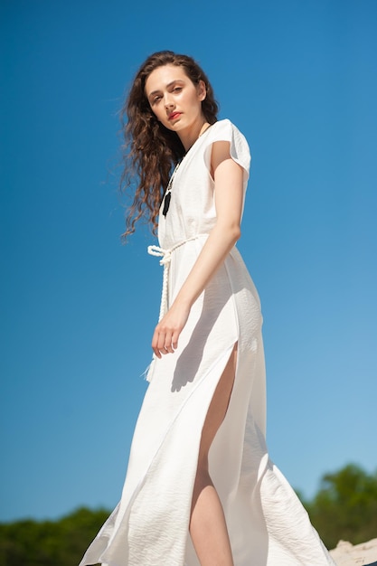 Una donna in abito bianco si trova su una collina di fronte a un cielo blu.