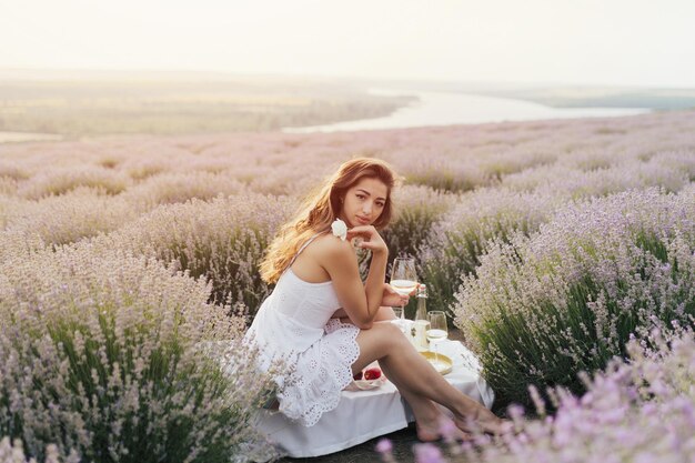 Una donna in abito bianco siede in un campo di lavanda.