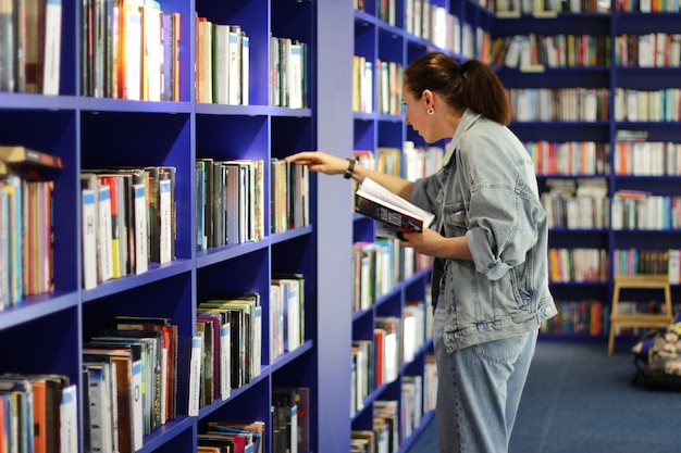 Una donna in biblioteca alla ricerca di un libro il concetto di educazione visita la sala di lettura