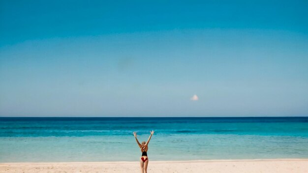 una donna in bikini è in piedi sulla spiaggia con le braccia in alto