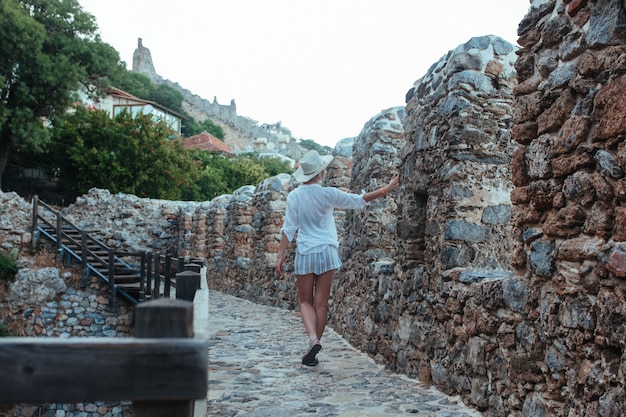 Una donna in camicia bianca e cappello cammina attraverso la fortezza di Alan