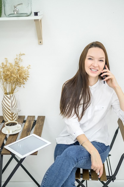 Una donna in camicia bianca e jeans siede in un bar e beve caffè Impiegata durante la pausa pranzo che parla al telefono Manager durante un incontro di lavoro in un ristorante