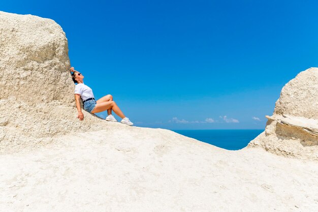 Una donna in canotta bianca e pantaloncini si siede su un'alta montagna di sabbia bianca e guarda il mare e il paesaggio sottostante contro un cielo blu brillante Ottima vista Turismo viaggi e attività ricreative