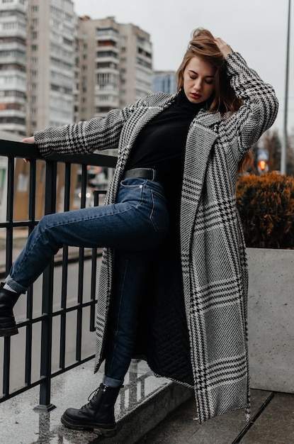 Una donna in cappotto e jeans si appoggia a una ringhiera