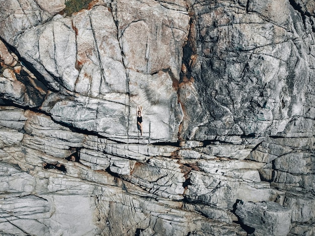 Una donna in costume da bagno nero sdraiata su una calda costa rocciosa fratturata, ripresa da un drone, sfondo.